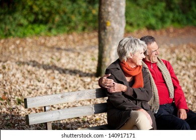 Smiling senior couple sitting on the bench park while looking at something - Powered by Shutterstock