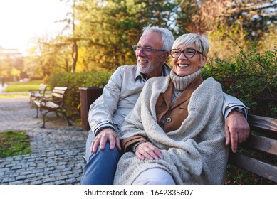 Smiling senior couple sitting on the bench in the park together enjoying retirement - Powered by Shutterstock