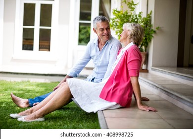 Smiling Senior Couple Sitting On Steps Outside House At Yard