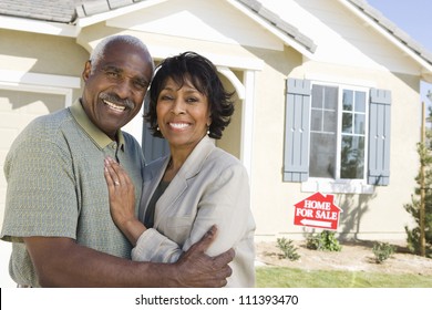 Smiling Senior Couple Standing In Front Of House For Sale