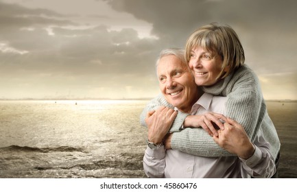 Smiling senior couple standing at the seaside at sunset - Powered by Shutterstock