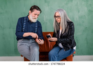 Smiling senior couple, stylish bearded man and pretty gray haired lady, enjoying review of photos on their smartphones, or showing each other how to use social networks - Powered by Shutterstock