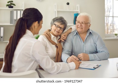 Smiling Senior Couple Talking To Nurse Or Their Family Practitioner Sitting At Table At Doctor's Office. Happy Mature Patients Listening To Physician Who's Explaining Prescribed Course Of Treatment