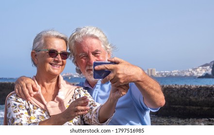 Smiling Senior Couple With White Hairs Having Fun With Smart Phone And Selfie - Horizon Over Water And Seascape - Concept Of Active Seniors During Holidays