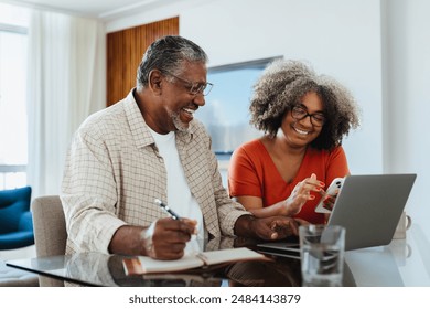 Smiling senior couple working on budget at home with a laptop and smartphone, discussing finances. - Powered by Shutterstock