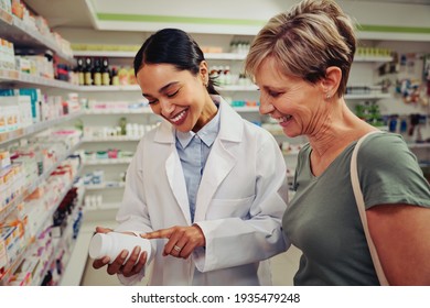 Smiling senior customer with pharmacist looking for medicinal details on bottle standing near shelves