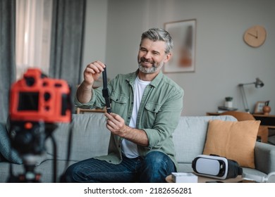 Smiling senior european male blogger records video review on technology and shows smart watch with empty screen in room interior. Hobbies and review of devices at home, modern blog for social media - Powered by Shutterstock