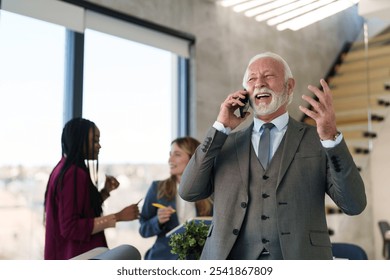 A smiling senior executive is actively engaged in a pleasant phone call, dressed in formal business attire, showcasing leadership within a modern office space, illuminated by natural light. - Powered by Shutterstock