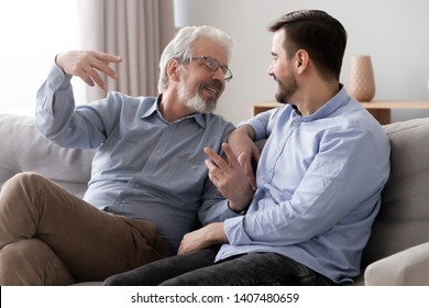 Smiling senior father sit on couch talk chat with millennial son spend time at home together, young man relax with elderly dad speak share thoughts have fun resting together on sofa in living room - Shutterstock ID 1407480659