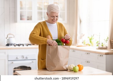 Smiling senior lady checking paper bag with grocery ordered from internet during COVID-19 quarantine, kitchen interior, copy space. Happy old woman unpacking purchase. Food delivery concept - Powered by Shutterstock
