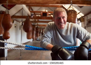 Smiling Senior Male Boxer In Gym Wearing Boxing Gloves Leaning On Ropes Of Boxing Ring - Powered by Shutterstock