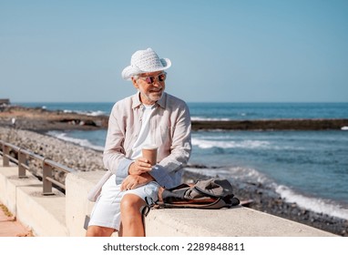 Smiling Senior Man at the Beach Looking Away Holding a Coffee Cup - Vacation Retirement Lifestyle concept at Sea - Relaxed Elderly Grandfather Enjoying Freedom and Good Time - Powered by Shutterstock