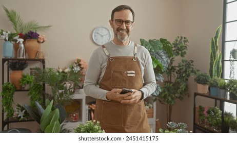 Smiling senior man with beard wearing apron using smartphone in vibrant flower shop - Powered by Shutterstock