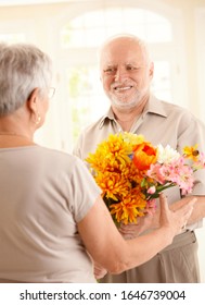 Smiling Senior Man Bringing Flowers To Older Woman.