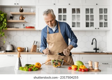 Smiling senior man cooking fresh vegetable salad in kitchen, adding olive oil and seasoning to bowl, elderly gentleman wearing apron making healthy vegetarian food at home, copy space - Powered by Shutterstock