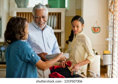 Smiling Senior Man Doing The Dishes With His Adult Daughter And Granddaughter.