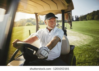 Smiling senior man driving a golf cart along a course while enjoying a round of golf on a sunny day - Powered by Shutterstock
