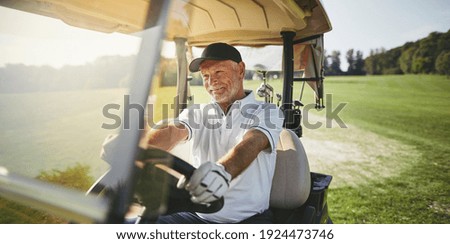 Smiling senior man driving a golf cart along a fairway while playing a round of golf on a sunny day
