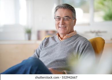 Smiling senior man with eyeglasses relaxing in armchair