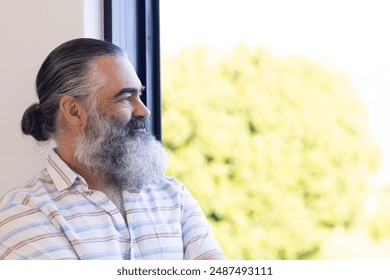 Smiling senior man with gray beard looking out window, enjoying peaceful moment, copy space. Happiness, tranquility, reflection, contemplation, wisdom, relaxation - Powered by Shutterstock