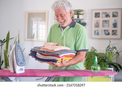 Smiling senior man helping with housework by ironing clothes on ironing board,  looking proud to his ironed and folded shirts - Shutterstock ID 2167318297
