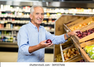 Smiling senior man holding red onion at the grocery - Powered by Shutterstock