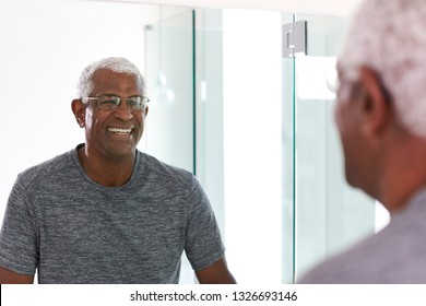 Smiling Senior Man Looking At Reflection In Bathroom Mirror Wearing Pajamas - Powered by Shutterstock