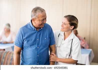 Smiling senior man looking at young female doctor at retirement home - Powered by Shutterstock