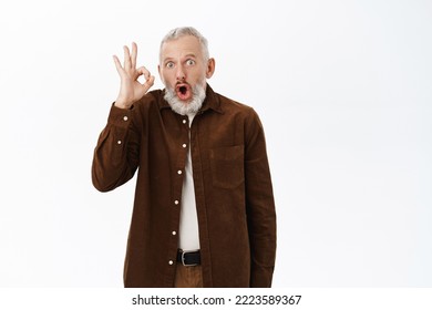 Smiling Senior Man, Mature Male Model Showing Okay Sign, Praise And Compliment, Recommending Smth Awesome, Standing Over White Background.