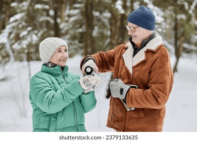 Smiling senior man pouring hot tea for wife when they are stand in winter forest - Powered by Shutterstock