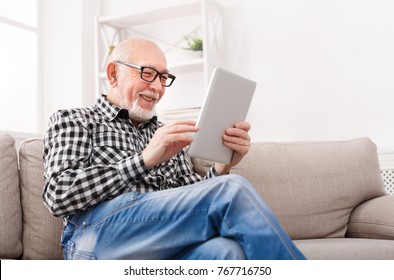 Smiling senior man reading news on digital tablet. Cheerful excited mature male using portable computer at home, copy space - Powered by Shutterstock