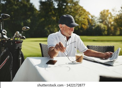 Smiling senior man relaxing at his golf club restaurant with a cup a coffee and a newspaper after playing a round of golf