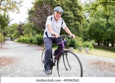Smiling Senior Man Riding Bicycle In Park