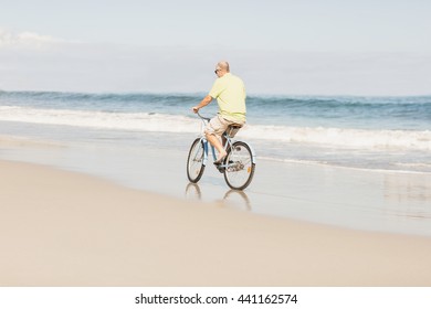 Smiling Senior Man Riding Bike On The Beach