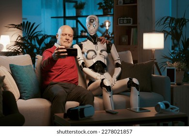 Smiling senior man sitting on the couch with his AI humanoid robot and taking pictures with his smartphone