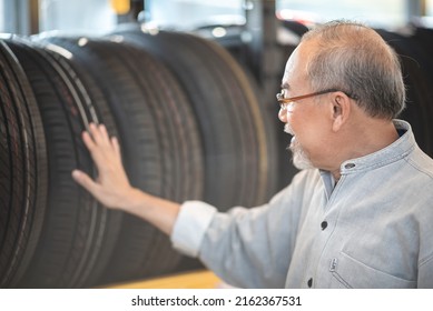 Smiling Senior Man With Spectacles And Beard Checking New Car Tires From Rack For Maintenance And Change In Garage While Getting Assistance From Young Male Mechanic