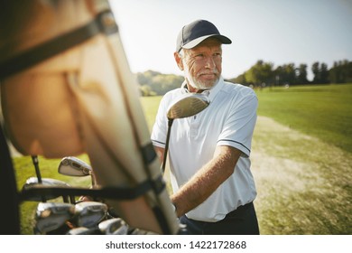 Smiling senior man standing by a golf cart looking out at the fairway while playing a round of golf on a sunny day - Powered by Shutterstock