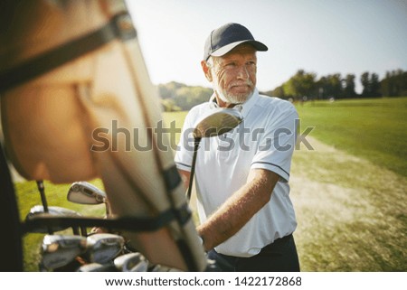 Smiling senior man standing by a golf cart looking out at the fairway while playing a round of golf on a sunny day