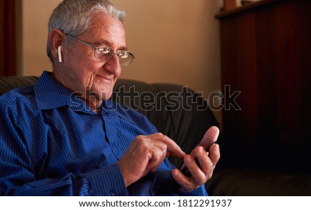 Smiling senior man using smart phone sat on sofa