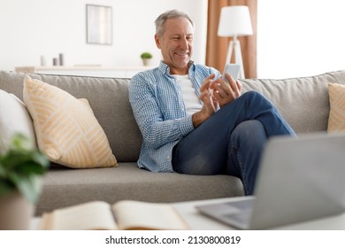 Smiling Senior Man Using Smartphone Texting Networking Online And Scrolling News Feed In Social Media Application Sitting On Couch At Home. Mature Male Reading Message On Phone. New Mobile App Concept - Powered by Shutterstock