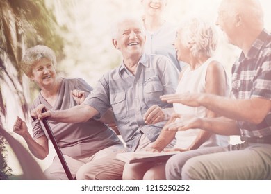 Smiling Senior Man With Walking Stick Relaxing With Elderly Woman And Friends