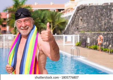 Smiling Senior Man With White Hair Comes Out Of The Pool Wearing Swimming Cap And Goggles Gesturing Ok With Hand - With A Colorful Towel On His Shoulders - Active Seniors In Retirement