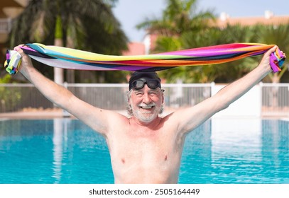 Smiling senior mature man while getting out of outdoor swimming pool wearing swimming cap and goggles holding towel. Caucasian retired man enjoying healthy and active life - Powered by Shutterstock