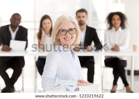 Smiling senior mature woman job applicant looks at camera at interview with hr recruiting team, happy middle aged lady business coach or vacancy candidate portrait, getting hired, employment concept