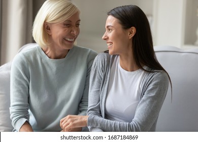 Smiling senior mother and grown-up adult daughter sit on couch at home gossip and talk, happy mature mom and millennial girl child relax on sofa in living room have fun, enjoy family weekend together