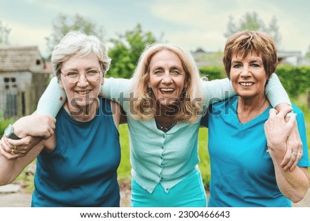 Smiling Senior Nordic Women After Outdoor Workout - Three happy women in their sixties embracing and smiling at the camera after a workout, posing in a countryside courtyard setting.
