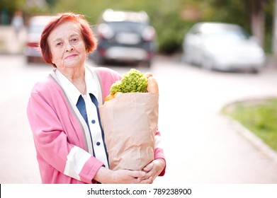 Smiling Senior Woman 70-80 Year Old Holding Shopping Bag With Food Walking Street. Looking At Camera. 