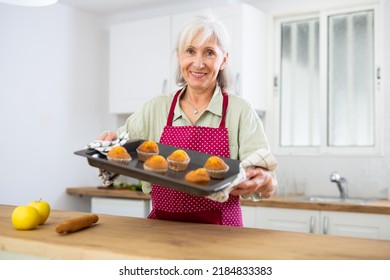 Smiling Senior Woman In Apron Holding Sheet Pan With Just Baked Cupcakes. Old Woman Baking Cakes At Home.