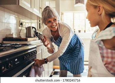 Smiling senior woman in apron opening the oven door. Happy granny and kid in kitchen cooking together.