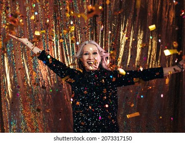 Smiling Senior Woman In Black Dress Having Fun Under Colorful Confetti Against A Golden Backdrop